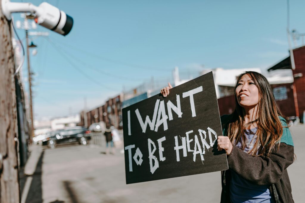 A woman holding a black handmade sign that says 'I WANT TO BE HEARD' during a public demonstration.