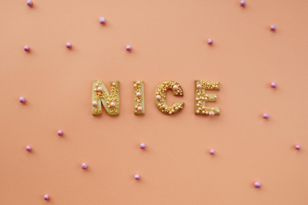 The word NICE spelled out in small pearls against a soft, solid peach-colored background.