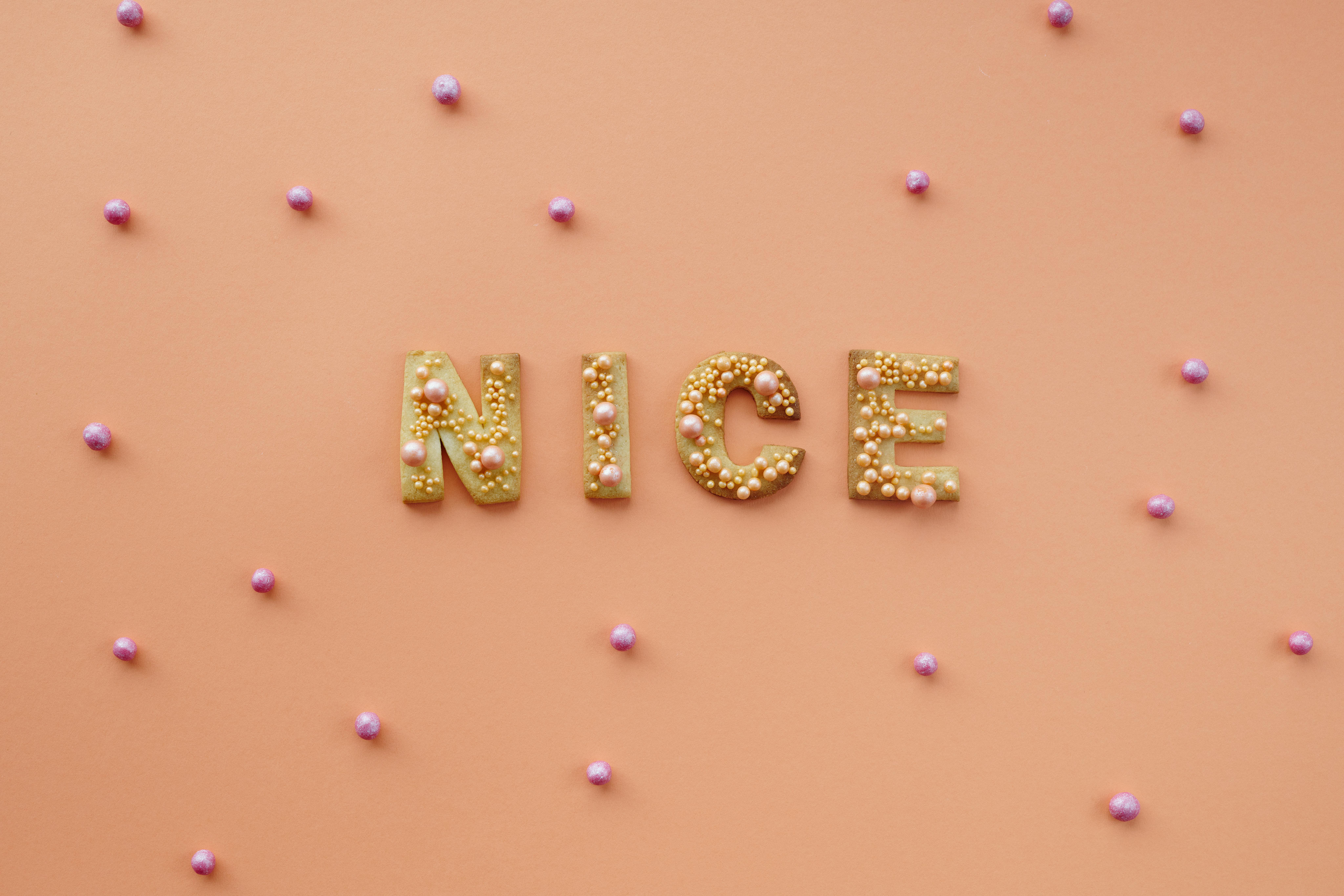 The word NICE spelled out in small pearls against a soft, solid peach-colored background.