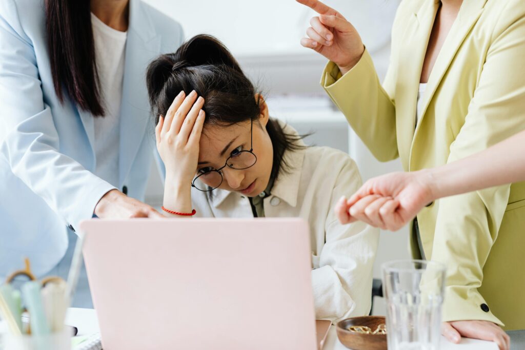 A woman sitting at a desk with her head in her hand, looking stressed and overwhelmed while working.