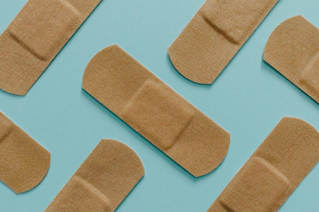 Three tan adhesive bandages (plasters) arranged on a clean, solid teal/blue background.