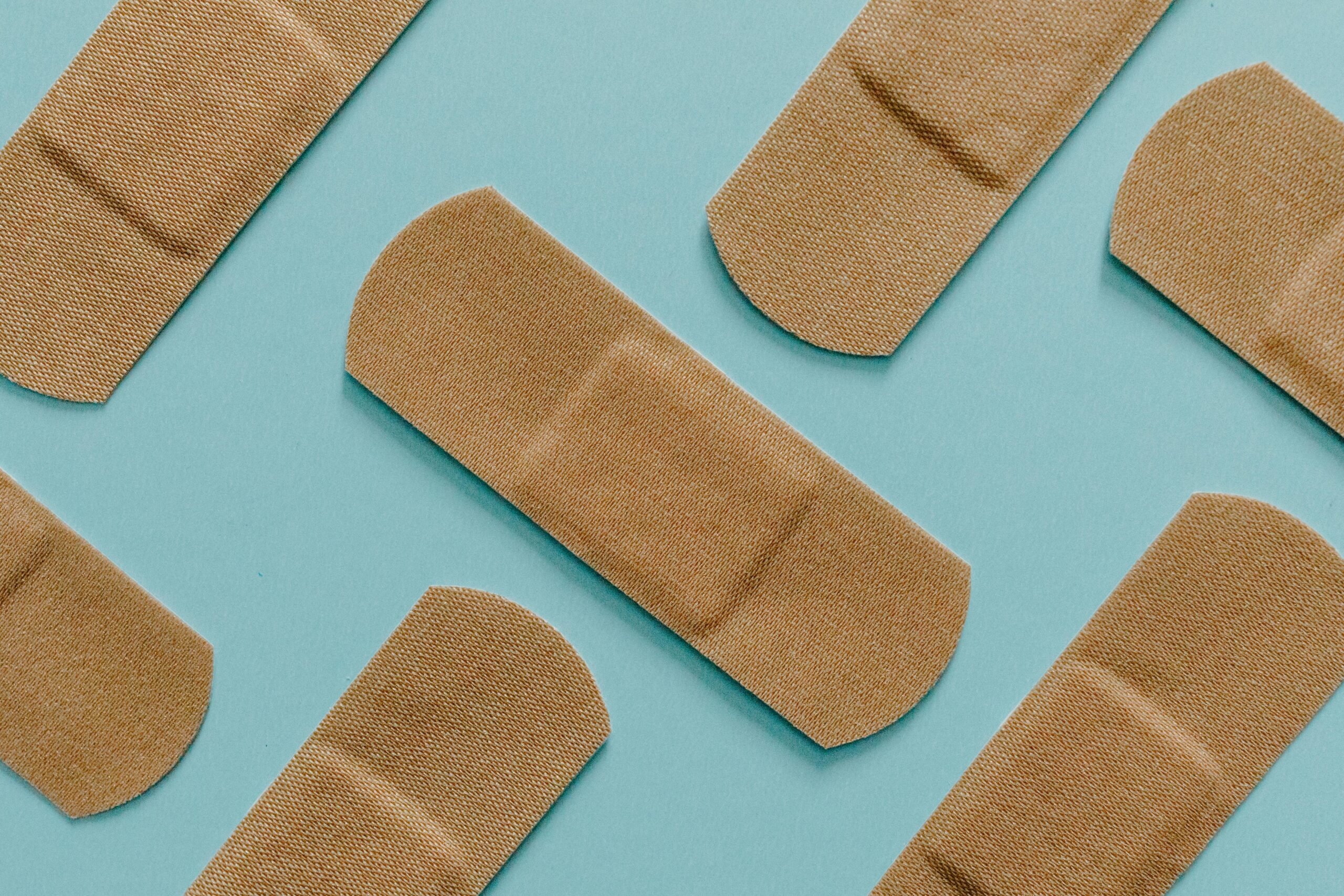 Three tan adhesive bandages (plasters) arranged on a clean, solid teal/blue background.