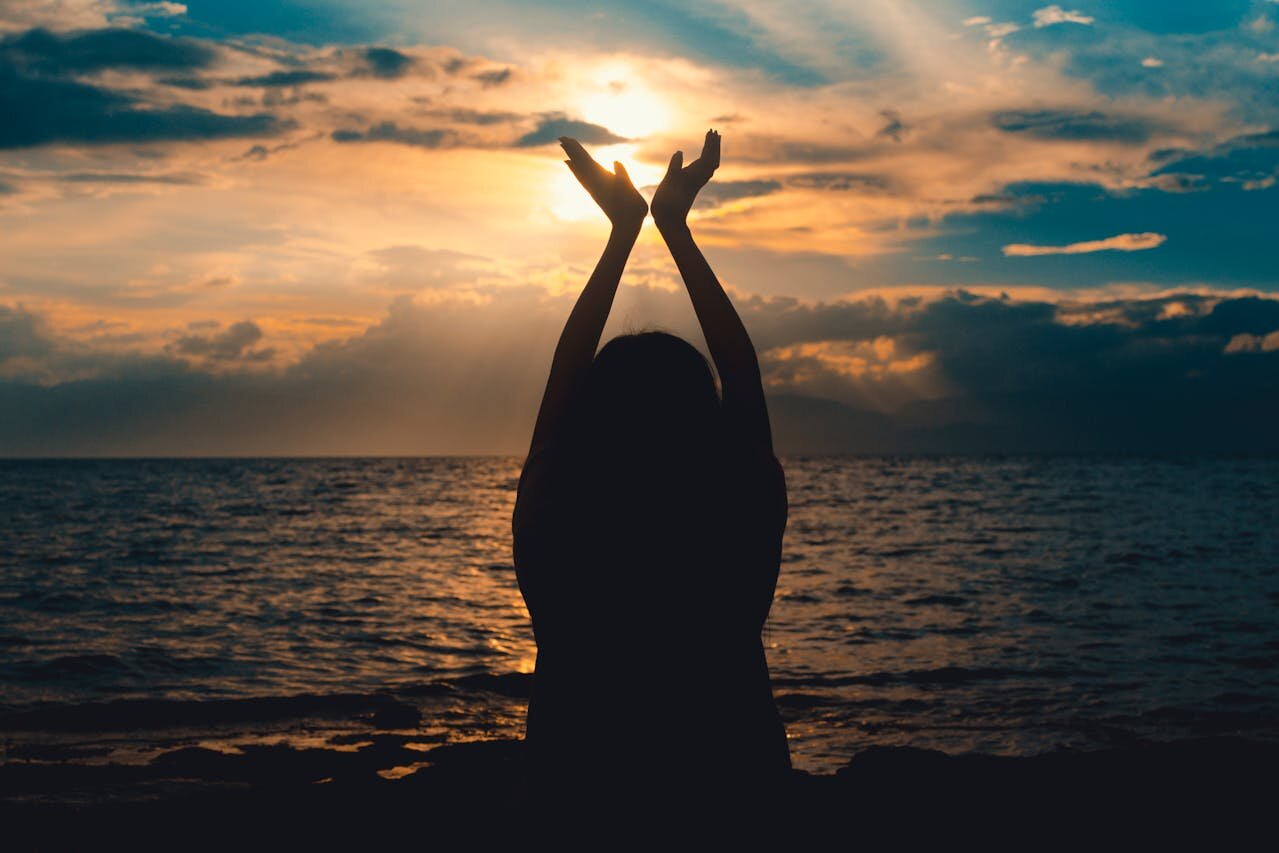 Woman silhouetted at sunset with raised arms during a clinical hypnosis and therapist self-regulation reflection practice